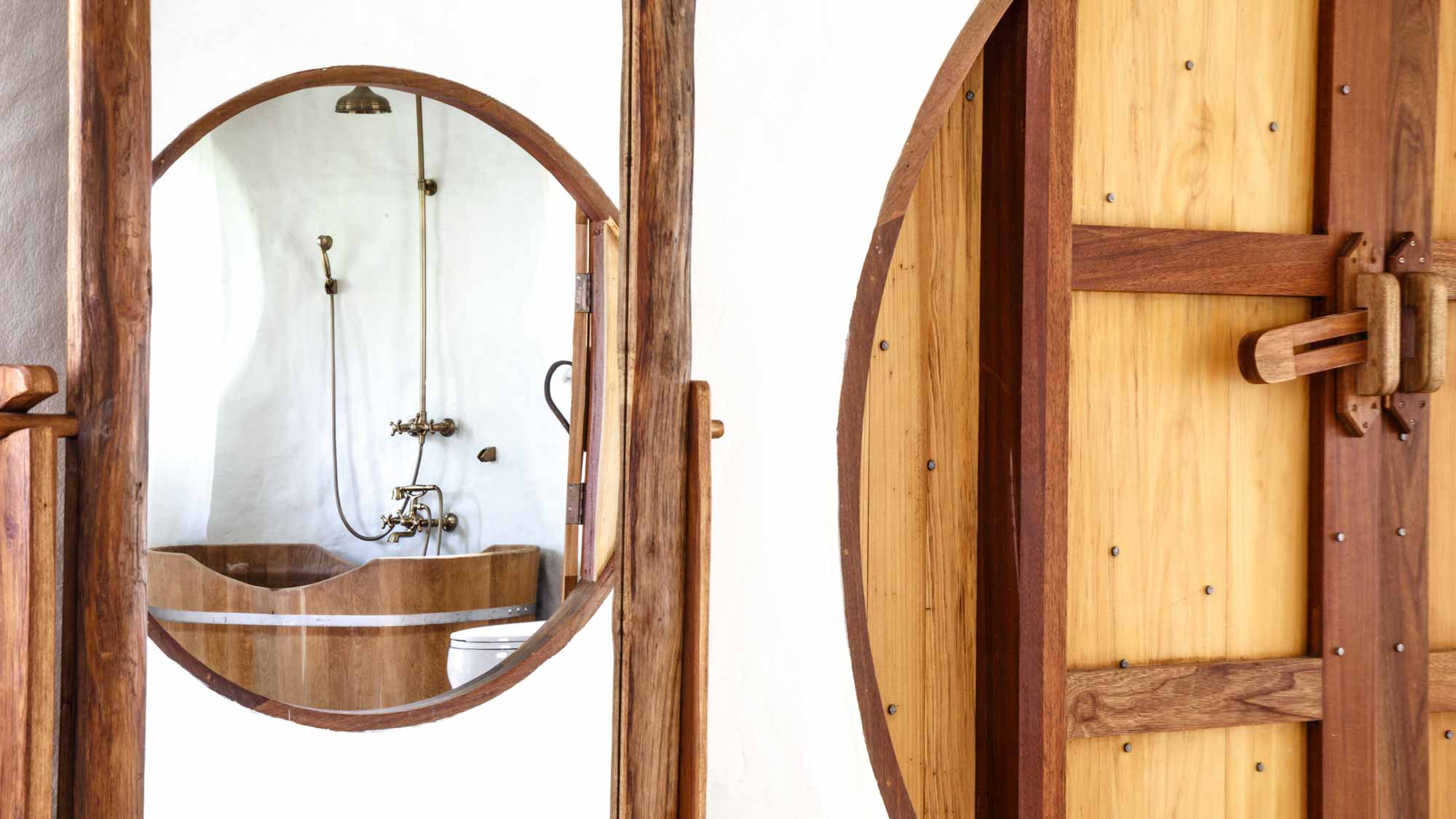 Looking through large round wooden doorway at a wooden bathtub and rain shower in the bathroom of the Hobbit Villa at the Mala Dhara Eco Resort and Yoga Retreat Center in chiang Mai Thailand.